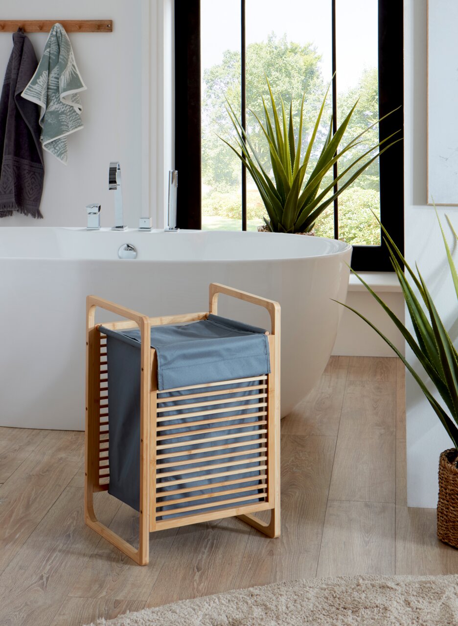 Bambus-Wäschekorb mit grauem Stoffeinsatz im modernen Badezimmer vor freistehender Badewanne, Frontansicht in leichter Schrägperspektive