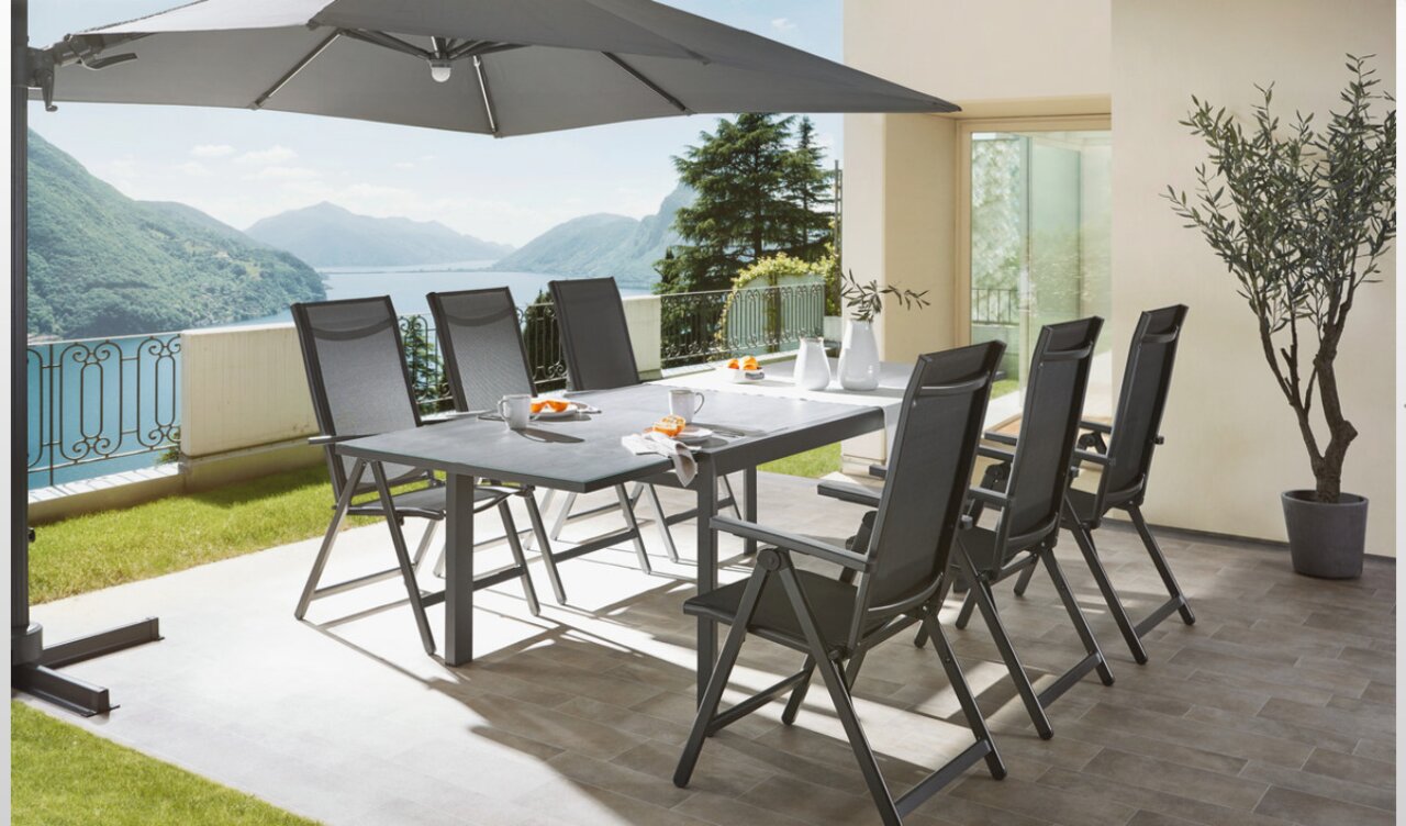 Ambia Garden Gartentisch TERUEL Moderner Gartentisch mit sechs Stühlen auf einer Terrasse mit Blick auf einen See, seitliche Perspektive.