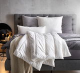 Gemütliches Solobett Vegan Dream 135x200 mit grauem Kopfteil, weißen und grauen Kissen sowie einer weißen Decke, seitliche Perspektive