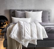 Gemütliches Solobett Vegan Dream 135x200 mit grauem Kopfteil, weißen und grauen Kissen sowie einer weißen Decke, seitliche Perspektive