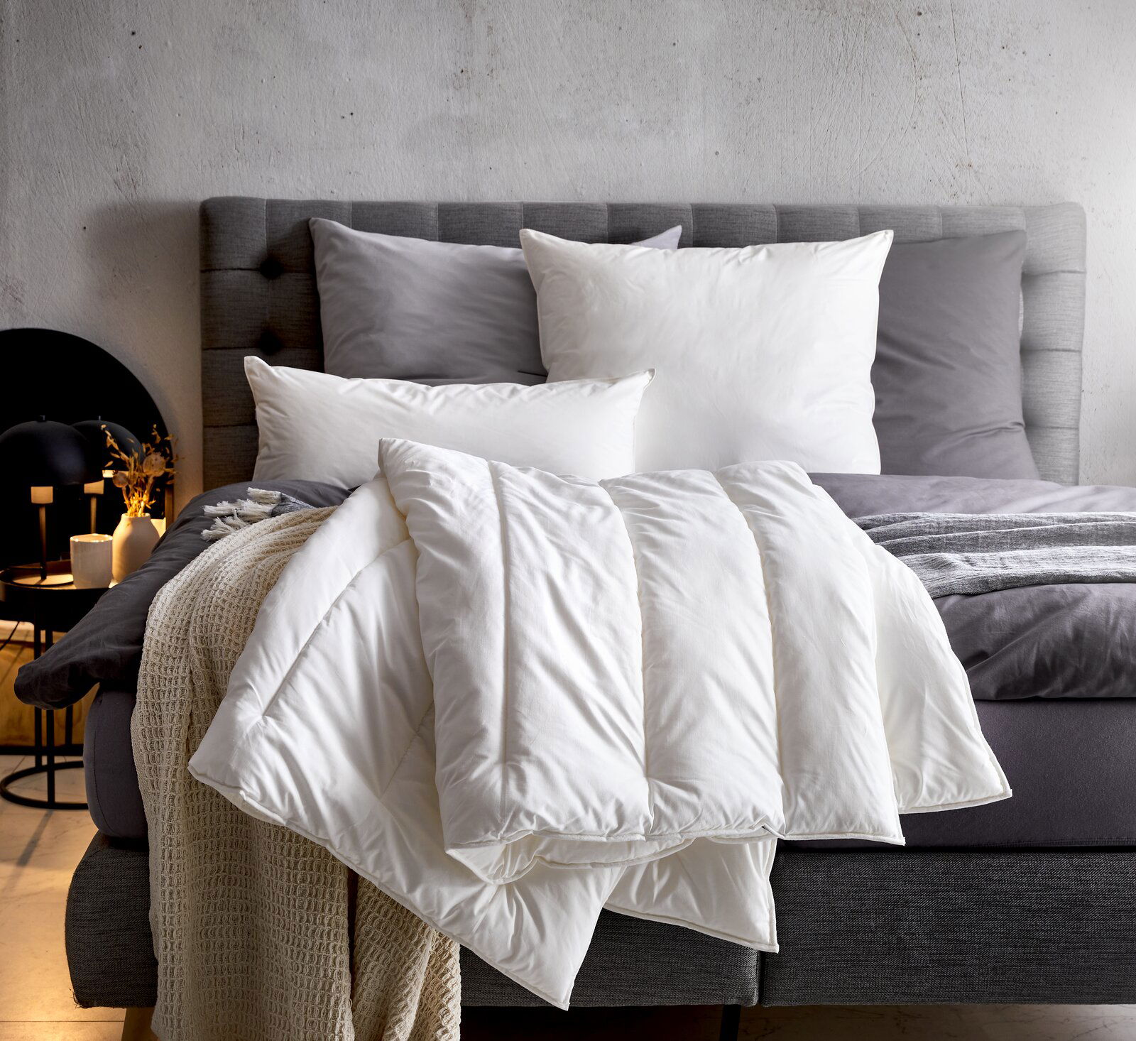 Gemütliches Solobett Vegan Dream 135x200 mit grauem Kopfteil, weißen und grauen Kissen sowie einer weißen Decke, seitliche Perspektive