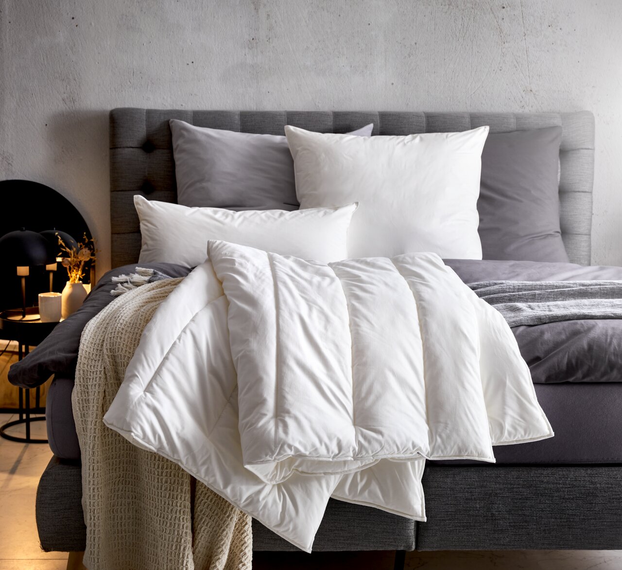 Gemütliches Solobett Vegan Dream 135x200 mit grauem Kopfteil, weißen und grauen Kissen sowie einer weißen Decke, seitliche Perspektive