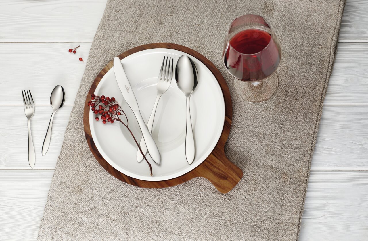 Besteckset Arthur 30-tlg. auf einem gedeckten Tisch mit Teller, Glas Rotwein und Dekoration aus roten Beeren, von oben betrachtet.
