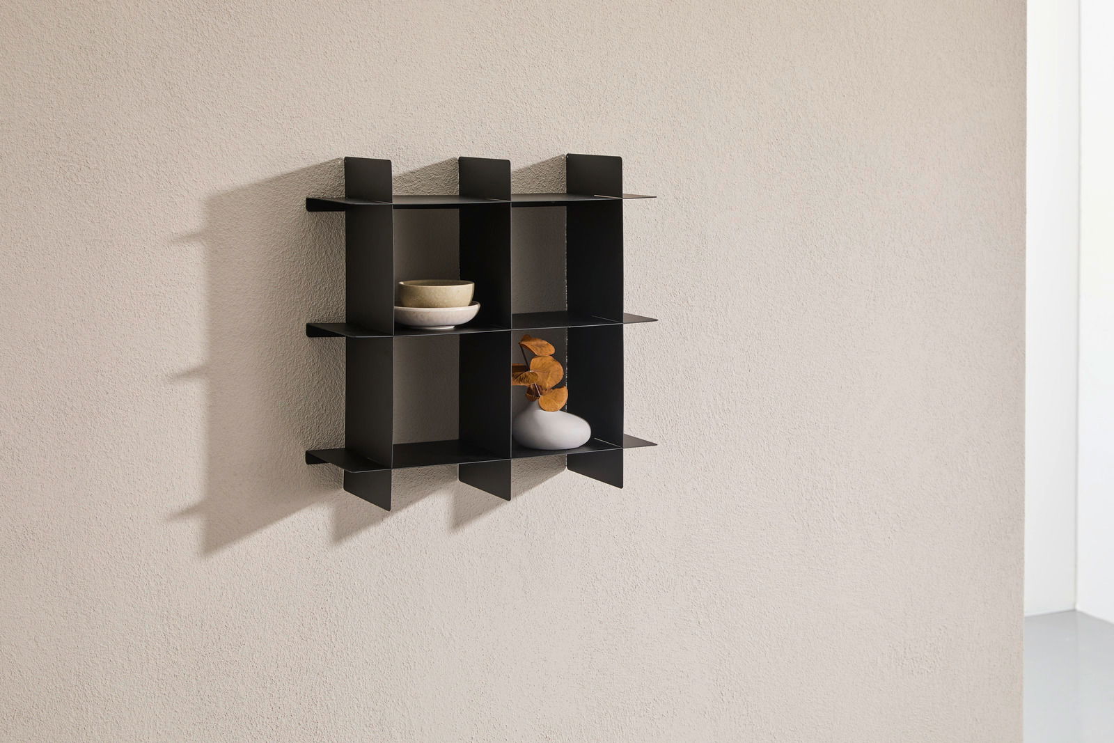 Schwarzes Wandregal mit mehreren Fächern, seitliche Perspektive, dekoriert mit Schalen und einer Vase.
