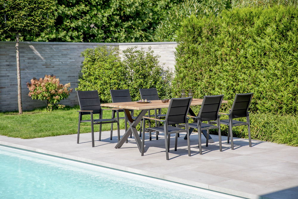 Gartenmöbel-Set mit sechs schwarzen Stühlen und einem Holztisch auf einer Terrasse am Pool, seitliche Perspektive