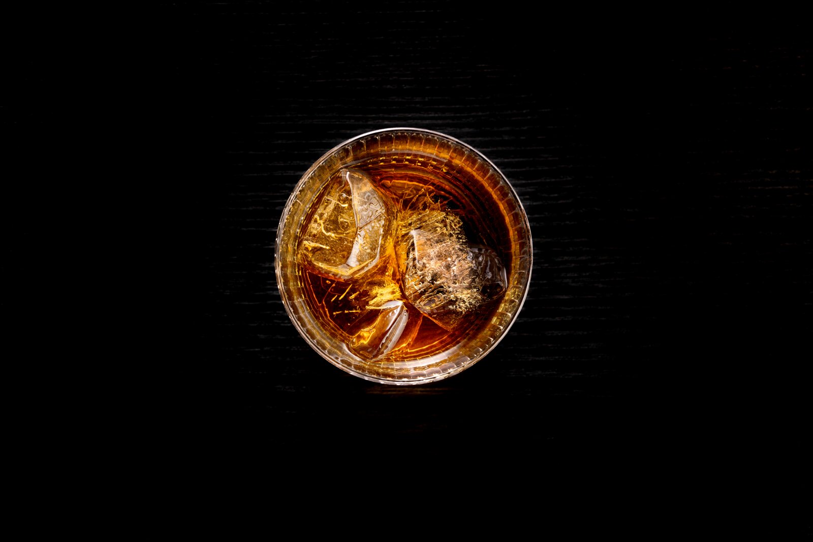 Ansicht von oben auf ein Glas mit einem Getränk und Eiswürfeln auf einem dunklen Holztisch.