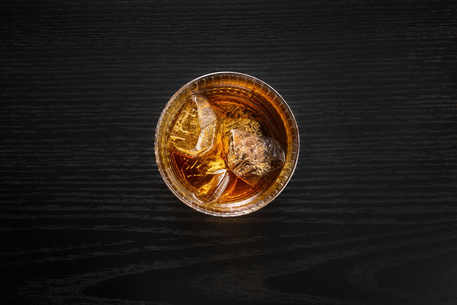 Ansicht von oben auf ein Glas mit einem Getränk und Eiswürfeln auf einem dunklen Holztisch.