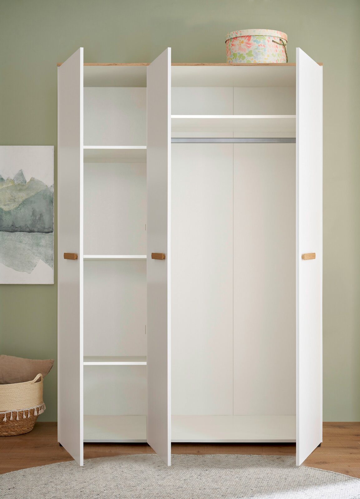 Offener weißer Kleiderschrank mit drei Türen, Holzgriffleisten und Kleiderstange sowie Regalfächern, frontale Perspektive.