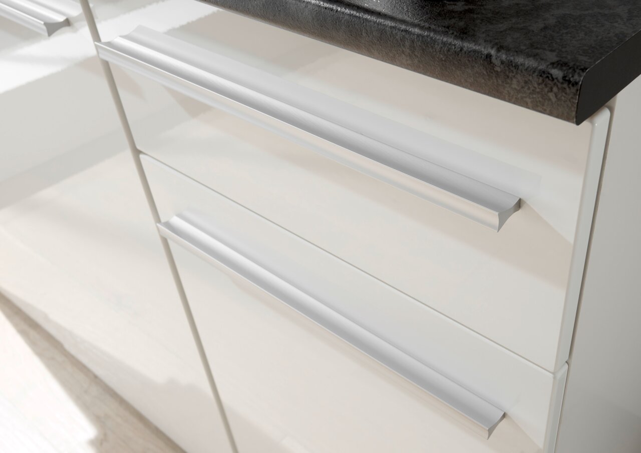 Nahaufnahme von weißen Küchenschubladen mit modernen, silbernen Griffen und einer dunklen Arbeitsplatte von oben betrachtet.