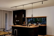 Moderne keuken met drie hangende Raja-decoratieve lampen in een elegante, donkere omgeving, gezien vanaf de zijkant.