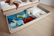 Bettkasten mit geöffnetem Schubfach, gefüllt mit bunten Decken, Kissen und Spielzeug, aus der Vogelperspektive fotografiert.