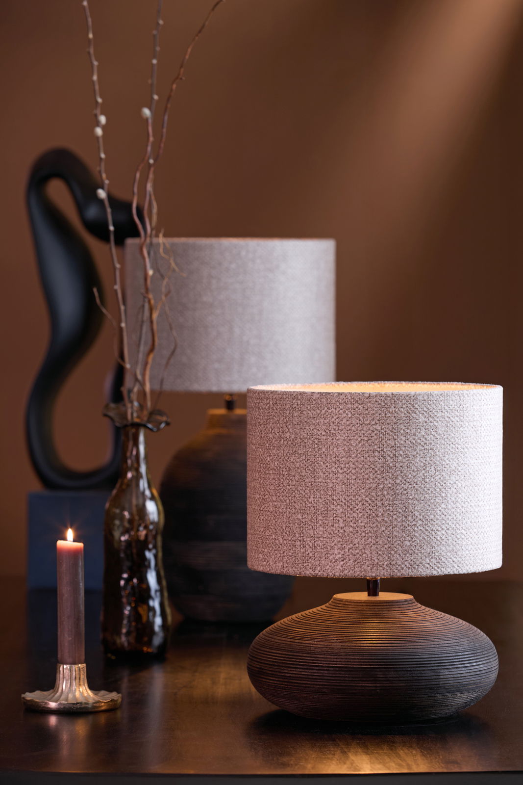 Stimmungsvolle Nahaufnahme eines Lampenfußes mit rundem, gerilltem Design und einem hellen Lampenschirm, im Hintergrund eine dekorative Vase und eine brennende Kerze.