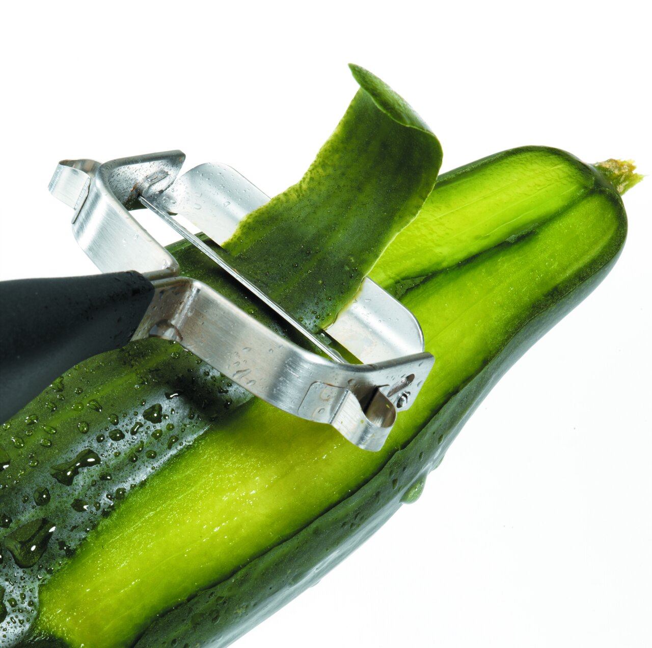 Nahaufnahme eines Sparschälers 'Universale', der eine Gurke schält. Der Sparschäler hat eine Metallklinge und einen schwarzen Griff.