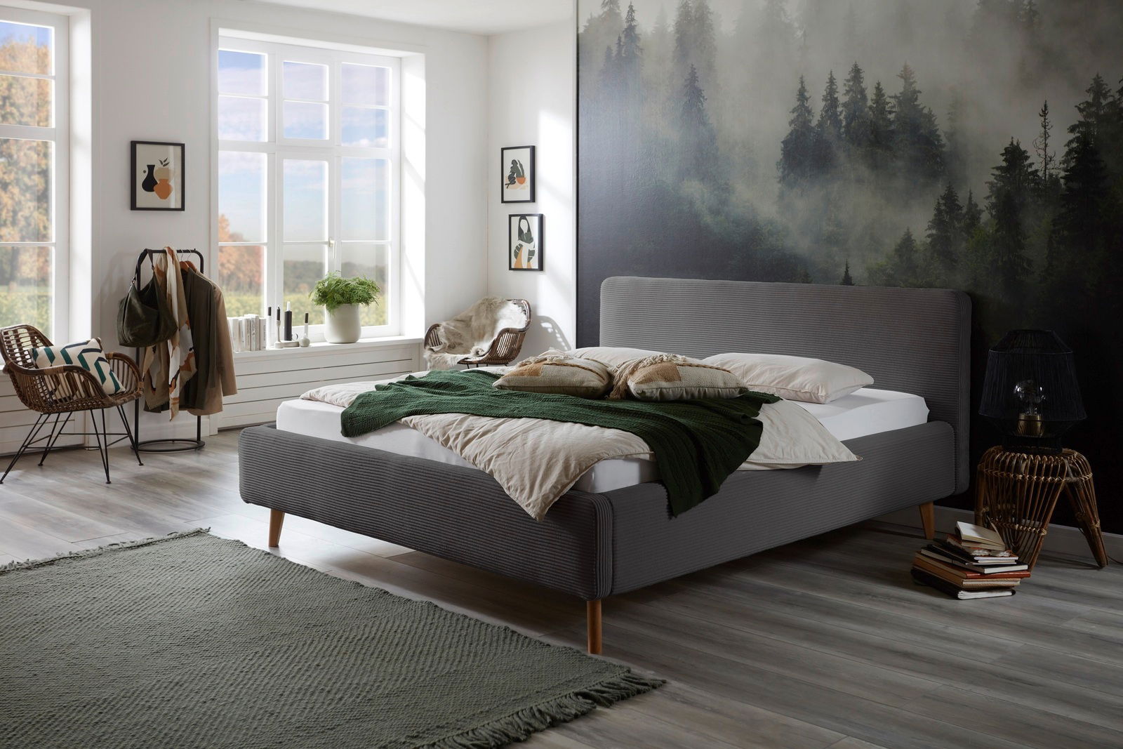 Modernes Polsterbettgestell in einem stilvoll eingerichteten Schlafzimmer mit Waldbild an der Wand, aus der Seitenperspektive fotografiert.