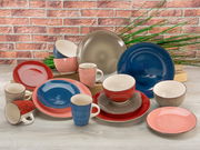Kombiservice 16-tlg. in verschiedenen Farben, bestehend aus Tellern, Schalen und Tassen, auf einem Tisch vor einer Ziegelwand ausgestellt. Perspektive: Frontalansicht.