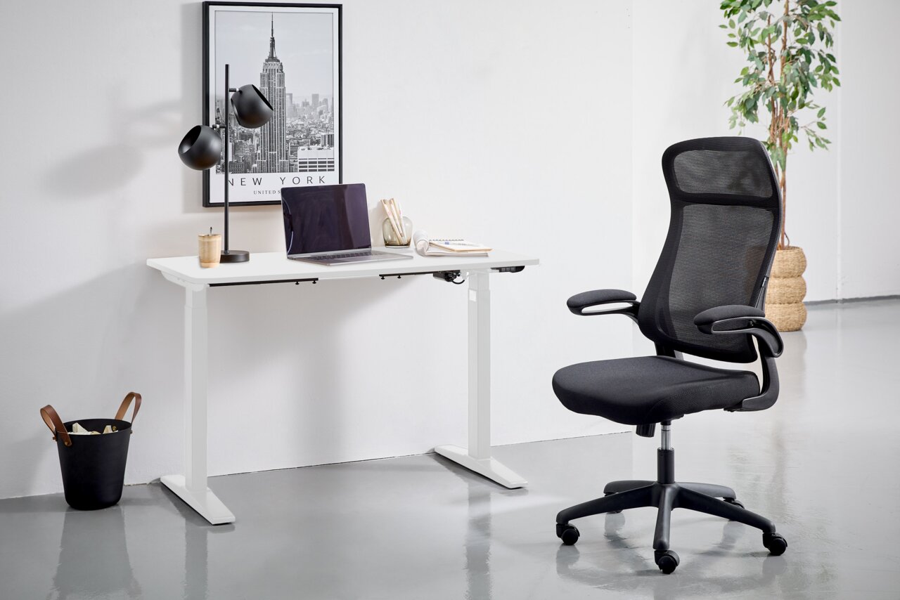 Moderner E-Schreibtisch in Weiß mit schwarzem Bürostuhl, seitliche Perspektive. Der Schreibtisch ist mit einer Lampe, einem Laptop und Schreibutensilien dekoriert. Im Hintergrund ein New York Poster und eine Pflanze.