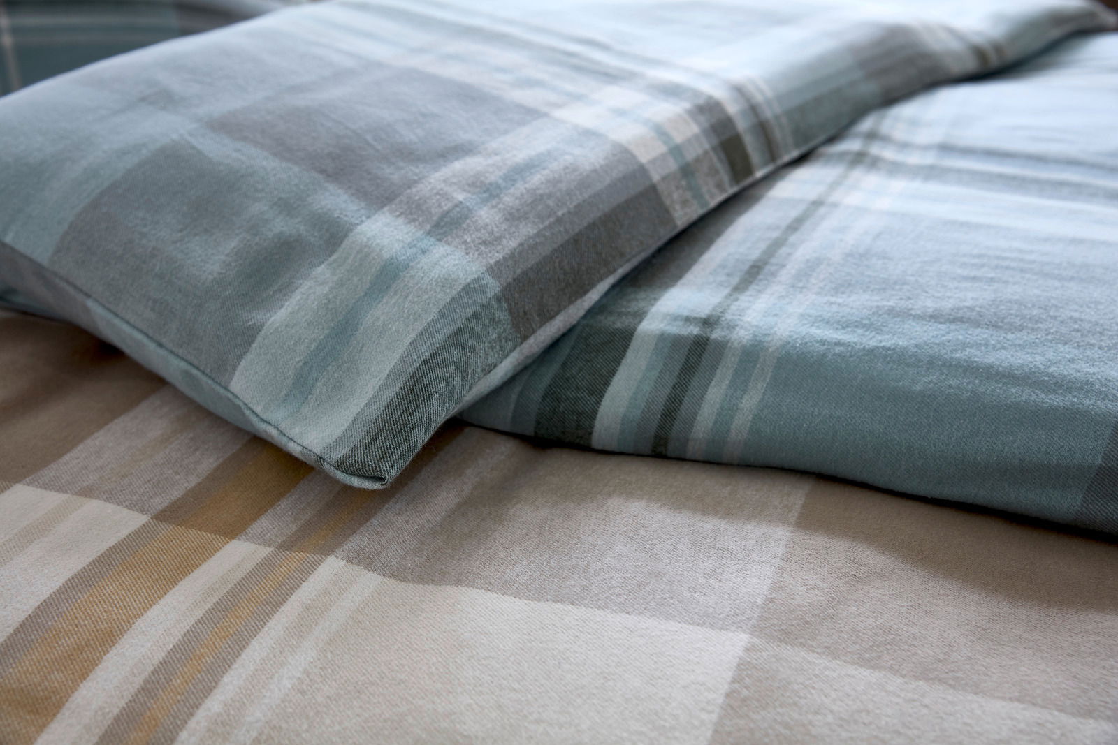 Nahaufnahme von Bettwäsche mit blau-grauem Karomuster, perspektivisch von der Seite aufgenommen.