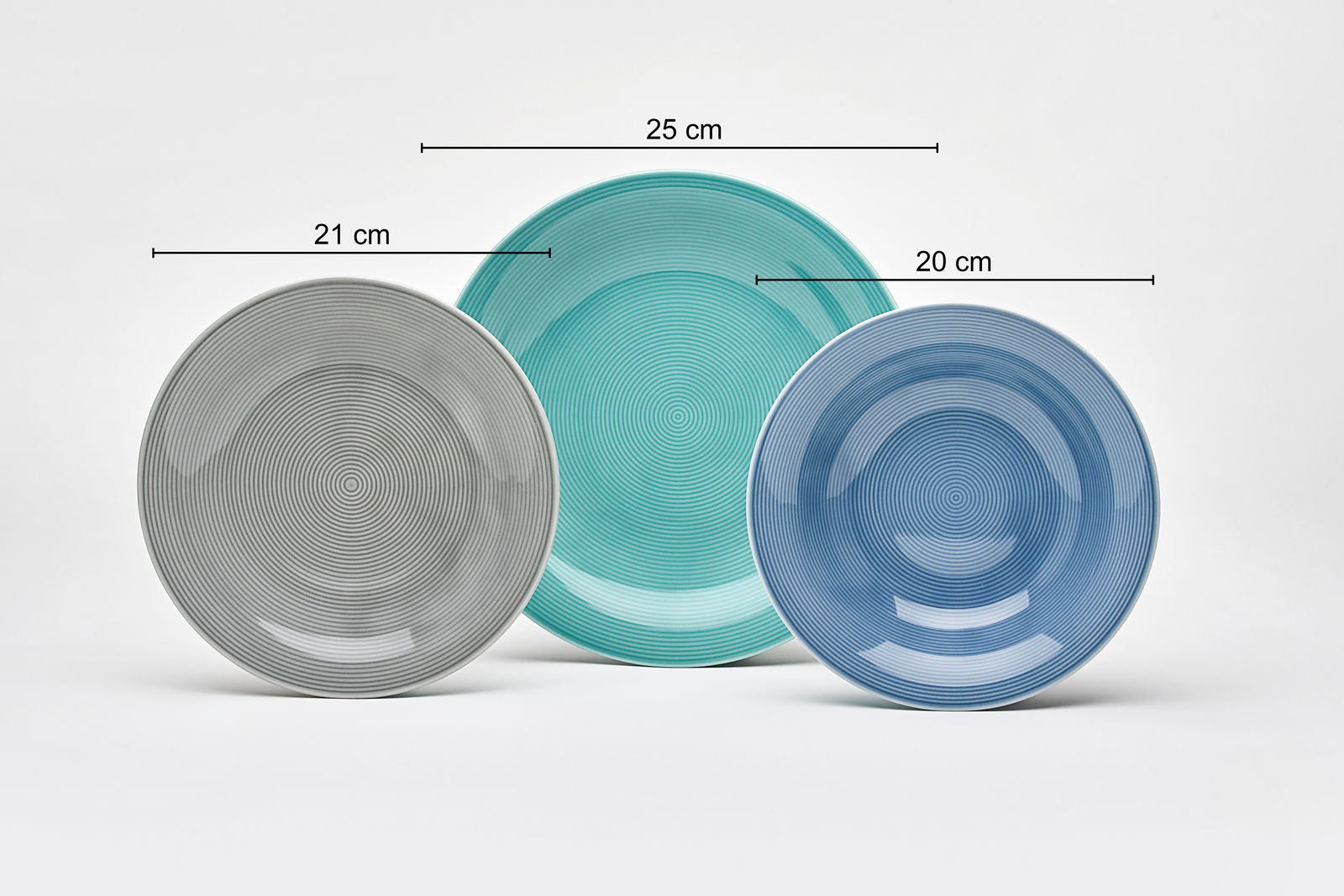 Drei Teller in verschiedenen Größen und Farben, von links nach rechts: grauer Teller (21 cm), grüner Teller (25 cm), blauer Teller (20 cm), aus der Vorderansicht fotografiert.
