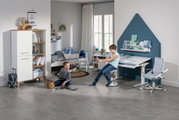 Modern bureau in een kinderkamer, gezien vanaf de zijkant, met een ergonomische stoel en een boekenkast, omringd door spelende kinderen.
