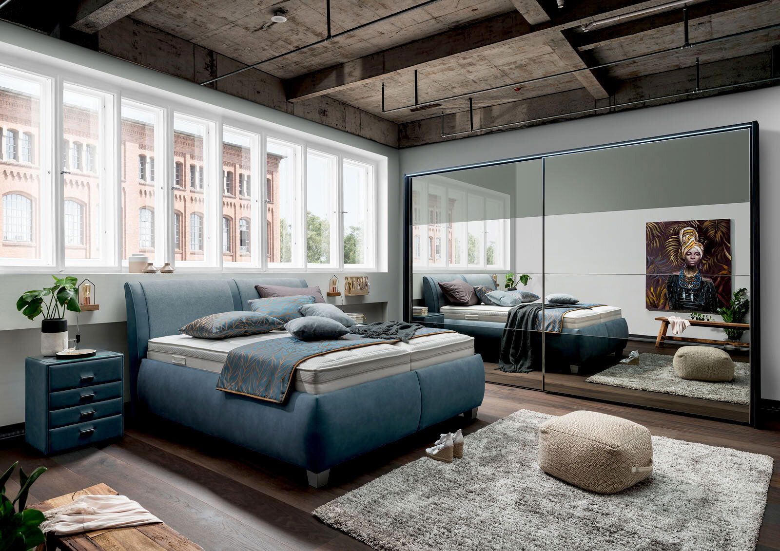 Modernes Polsterbett in einem stilvollen Schlafzimmer mit großen Fenstern und einem Spiegel, der den Raum reflektiert. Perspektive von der Seite.