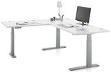 Moderner weißer E-Eckschreibtisch mit höhenverstellbaren Beinen, ausgestattet mit Monitor, Tastatur, Maus und Schreibtischlampe, aus seitlicher Perspektive.