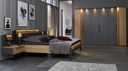Moderne slaapkamer in hout- en grijstinten, bestaande uit een bed met ingebouwde nachtkastjes, sierkussens en een grote kledingkast, gezien vanaf de zijkant.