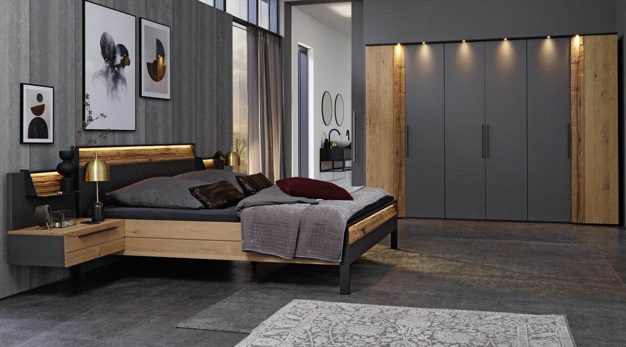 Moderne slaapkamer in hout- en grijstinten, bestaande uit een bed met ingebouwde nachtkastjes, sierkussens en een grote kledingkast, gezien vanaf de zijkant.