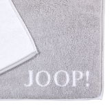 Graue Badematte mit weißem Rand und dem Schriftzug 'JOOP!' in der unteren rechten Ecke, aus der Vogelperspektive fotografiert.