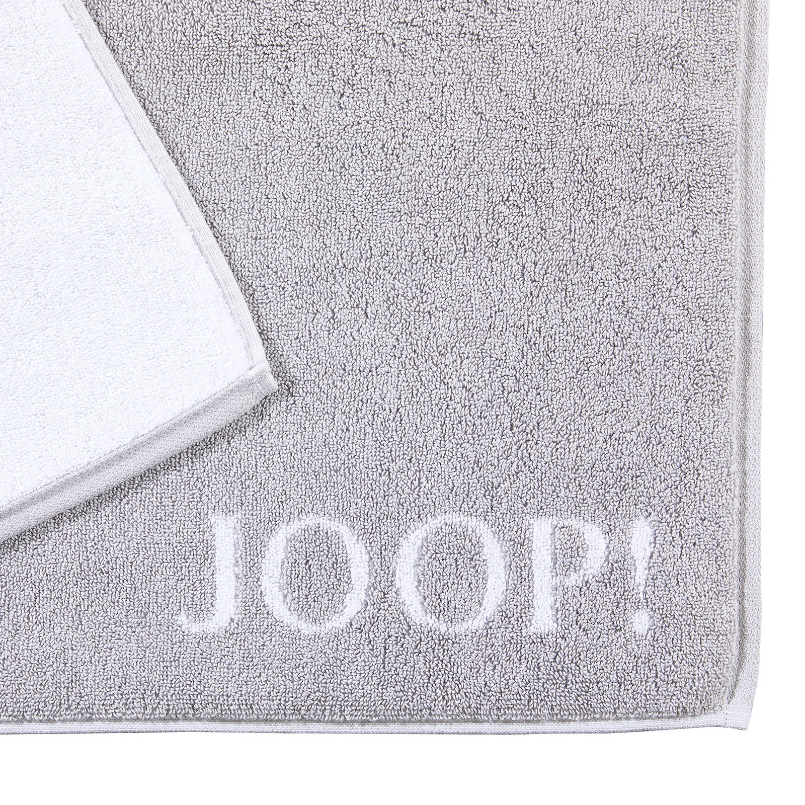 Graue Badematte mit weißem Rand und dem Schriftzug 'JOOP!' in der unteren rechten Ecke, aus der Vogelperspektive fotografiert.