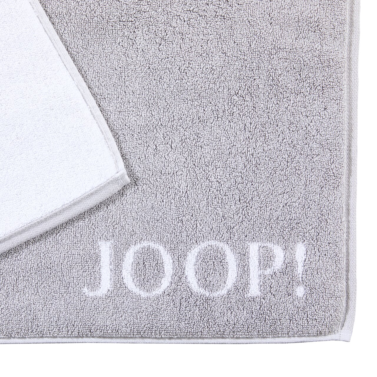 Graue Badematte mit weißem Rand und dem Schriftzug 'JOOP!' in der unteren rechten Ecke, aus der Vogelperspektive fotografiert.