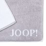 Graue Badematte mit weißem Rand und dem Schriftzug 'JOOP!' in der unteren rechten Ecke, aus der Vogelperspektive fotografiert.