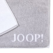 Graue Badematte mit weißem Rand und dem Schriftzug 'JOOP!' in der unteren rechten Ecke, aus der Vogelperspektive fotografiert.