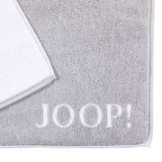 Graue Badematte mit weißem Rand und dem Schriftzug 'JOOP!' in der unteren rechten Ecke, aus der Vogelperspektive fotografiert.