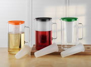 Drei Krüge mit farbigen Deckeln in Orange, Schwarz und Grün, jeweils mit Eiseinsatz und Sieb, auf einem Tisch von vorne fotografiert.