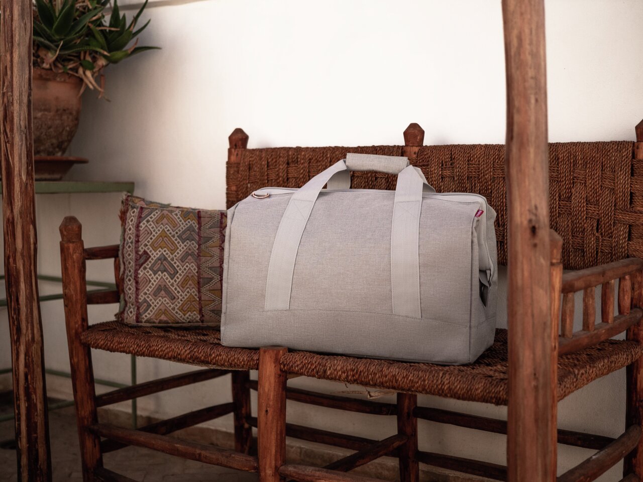 Reisenthel Allrounder L Twist Sky Rose Graue Reisetasche auf einem rustikalen Holzstuhl, seitliche Perspektive