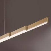Moderne, lineare LED-Pendelleuchte in Gold/Champagner mit durchgehendem Diffusor, schräg von unten in Nahaufnahme vor grauem Hintergrund fotografiert.