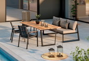 Moderne Outdoor-Loungegruppe auf einer Terrasse am Pool: rechteckiger Holztisch mit dunklem Metallgestell, zwei Seilstühle und ein graues 2-Sitzer-Sofa mit Kissen, dekoriert mit Kerzen und Pflanze, aufgenommen in schräger Frontansicht.