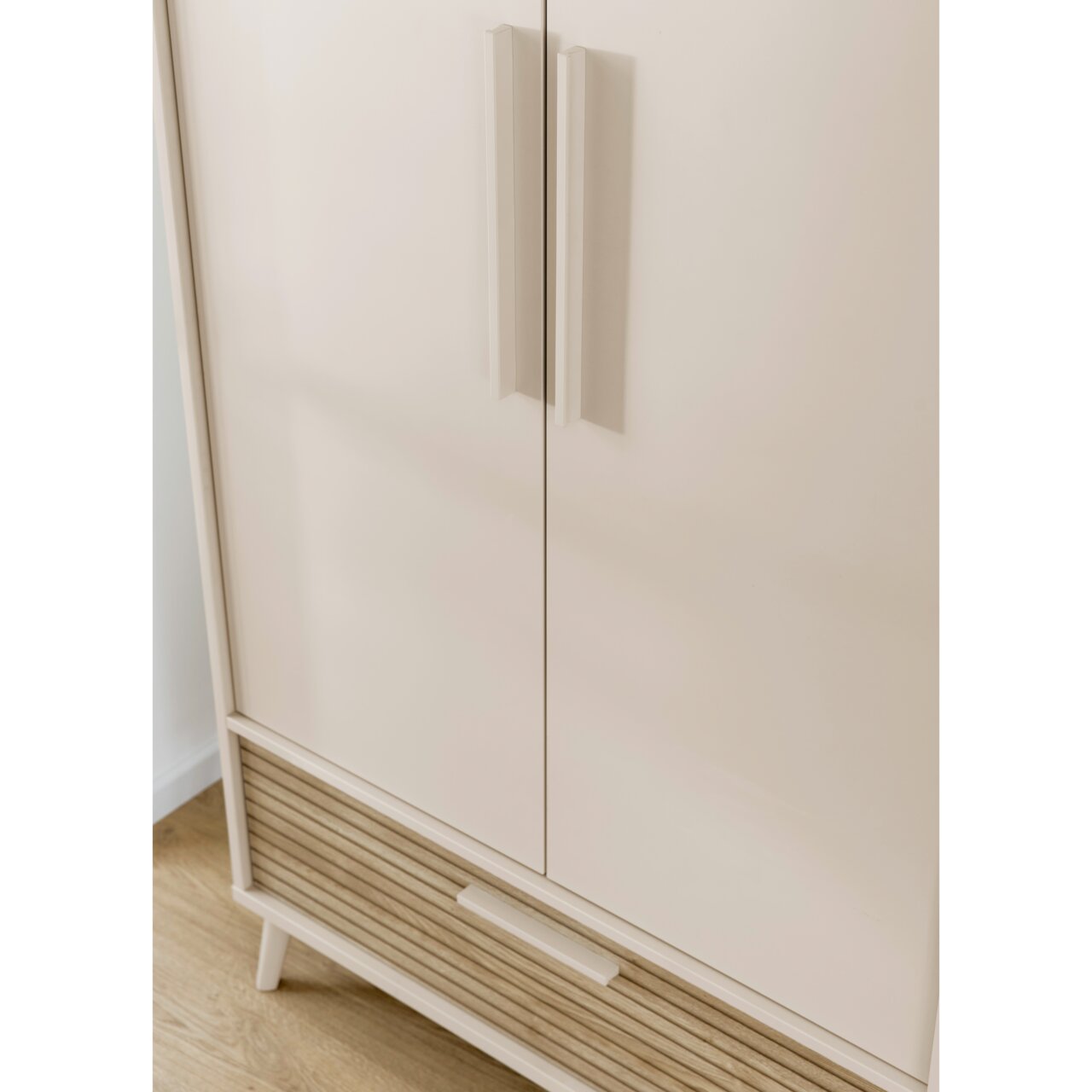 Nahaufnahme eines modernen Kleiderschranks mit zwei Türen und einer Schublade, in heller Farbe mit Holzdetails, aus der Vorderansicht.