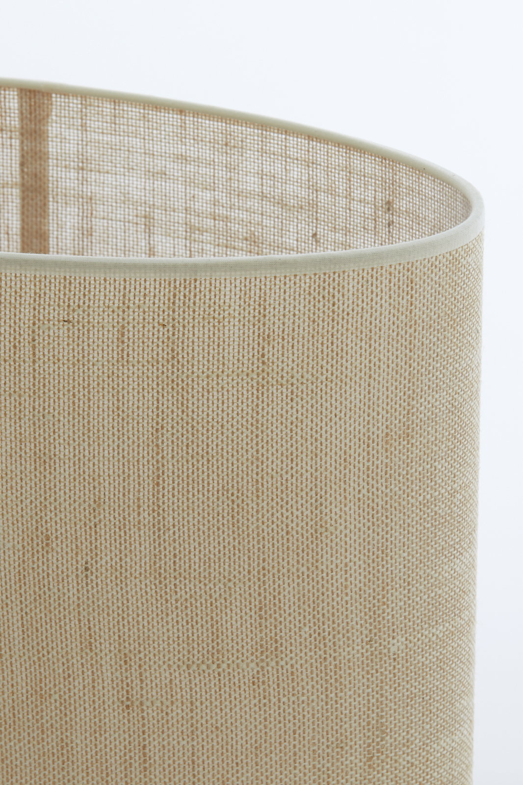 Nahaufnahme eines ovalen, geraden Lampenschirms aus beigem Stoff mit feiner Textur, seitliche Perspektive