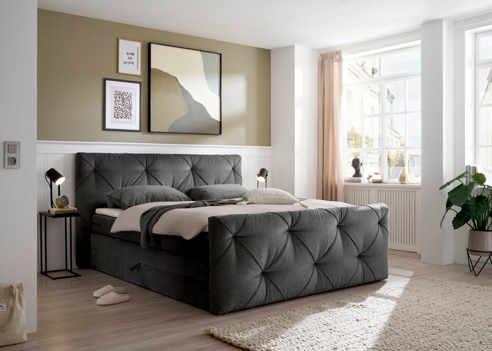 Graues Boxspringbett in einem hellen Schlafzimmer, seitliche Perspektive