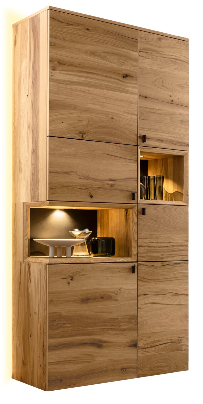 Venjakob Vitrine ANDIAMO 3.0 Hoher Massivholz-Schrank aus Eiche mit natürlicher Maserung, mehreren Türen und offenen, beleuchteten Nischen mit Dekoobjekten, fotografiert in leicht schräger Frontansicht von links.