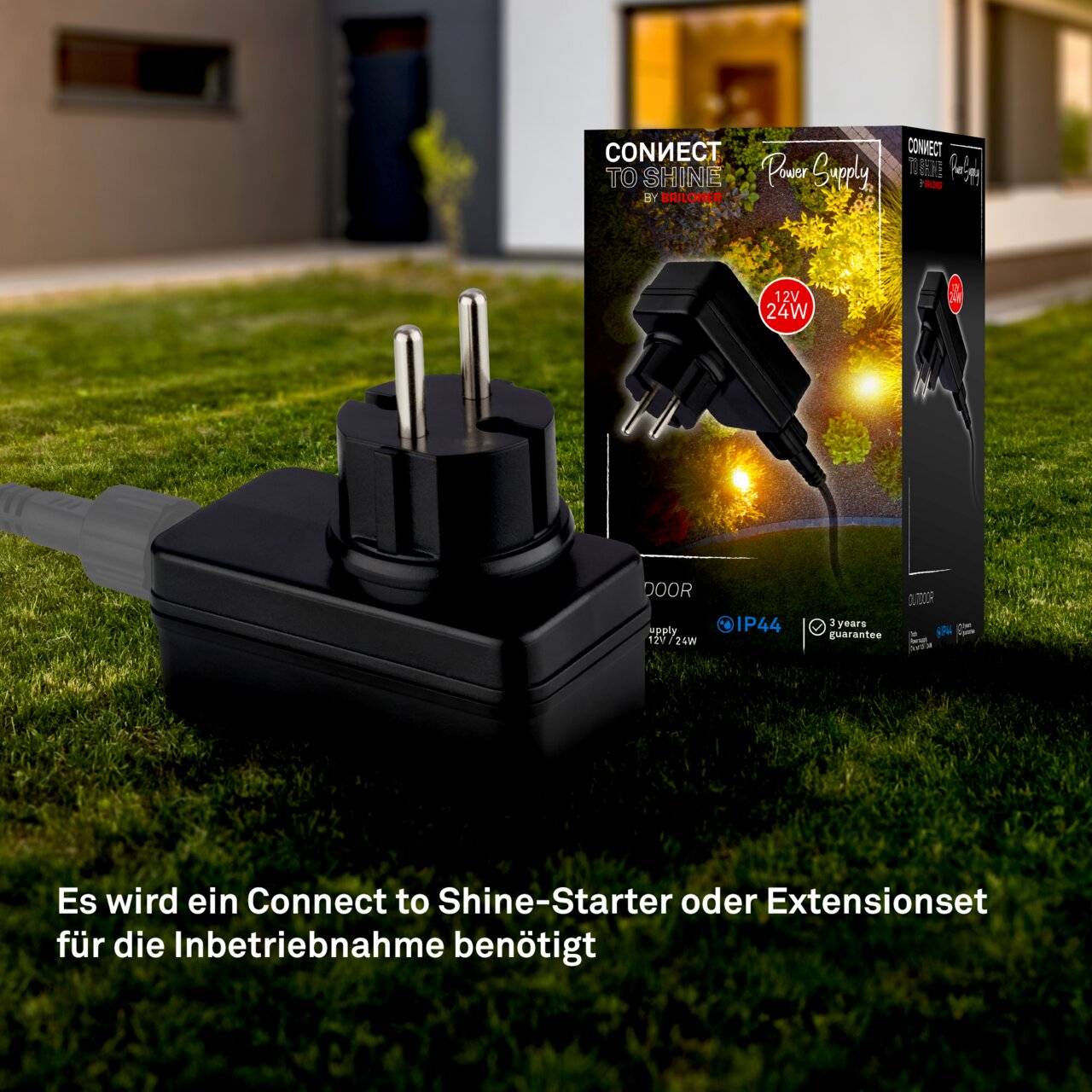 Briloner Treiber-Transformator GARTENSYSTEM Treiber-Transformator IP44, 24W, in Nahaufnahme auf einer Wiese vor einem modernen Haus, mit Verpackung im Hintergrund.