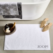 Weiße Badematte mit 'JOOP!' Schriftzug, platziert vor einer Badewanne, mit dekorativen Elementen wie einem Korb und Hausschuhen. Draufsicht.