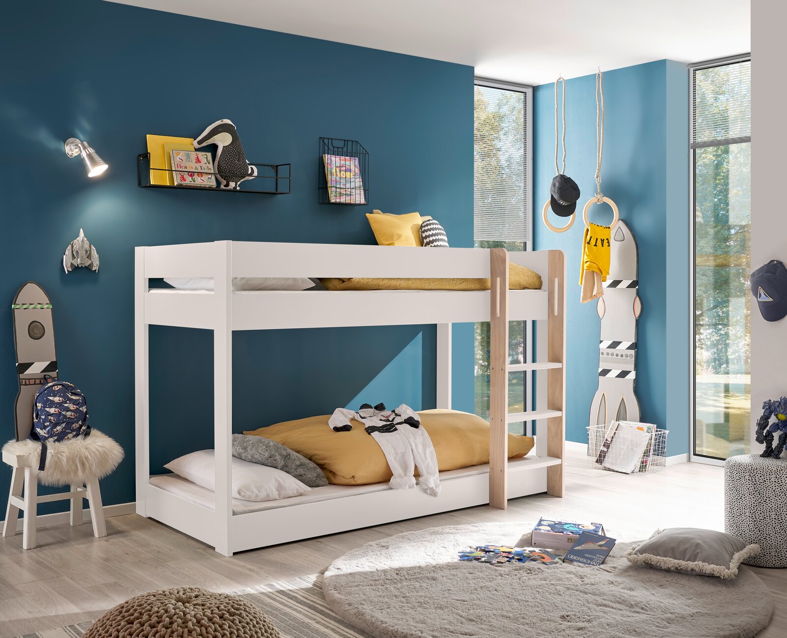 Weißes Etagenbett in einem modernen Kinderzimmer mit blauer Wand, dekoriert mit Spielzeug und Büchern. Perspektive von der Seite.