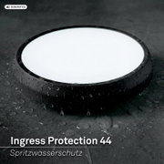 Ronde zwarte LED-lamp met witte diffuser en waterdruppels, spatwaterdicht IP44, gefotografeerd in schuin bovenaanzicht op natte donkere ondergrond