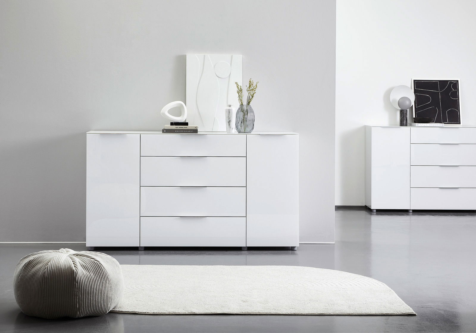 Weißes Sideboard mit drei Schubladen und zwei Türen, dekoriert mit modernen Accessoires, aus frontaler Perspektive fotografiert.