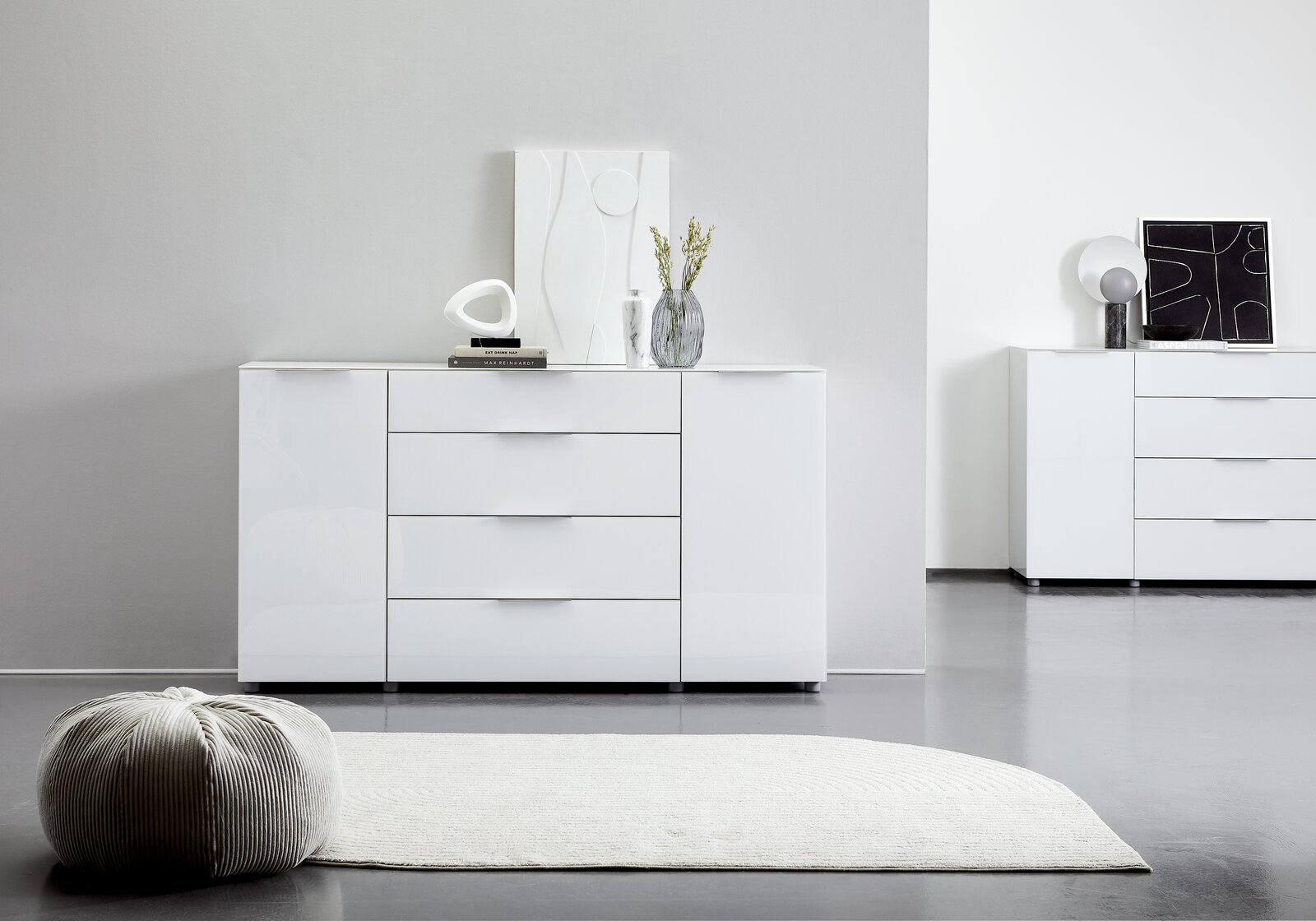 Weißes Sideboard mit drei Schubladen und zwei Türen, dekoriert mit modernen Accessoires, aus frontaler Perspektive fotografiert.