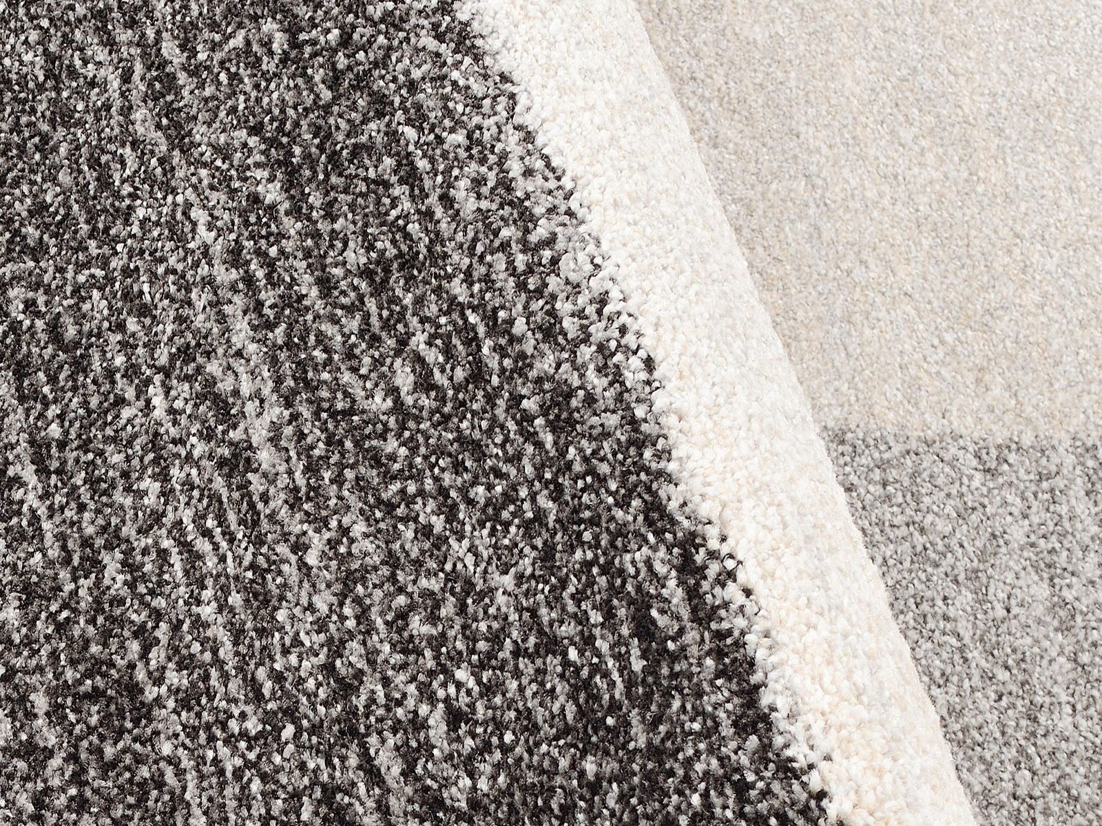 Nahaufnahme eines Teppichs mit gemustertem Design in Grautönen, perspektivisch von oben fotografiert.
