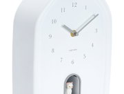Weiße Wanduhr mit minimalistischen Ziffern und einer kleinen Katzenfigur in einer Nische, seitliche Perspektive
