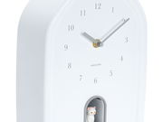 Weiße Wanduhr mit minimalistischen Ziffern und einer kleinen Katzenfigur in einer Nische, seitliche Perspektive